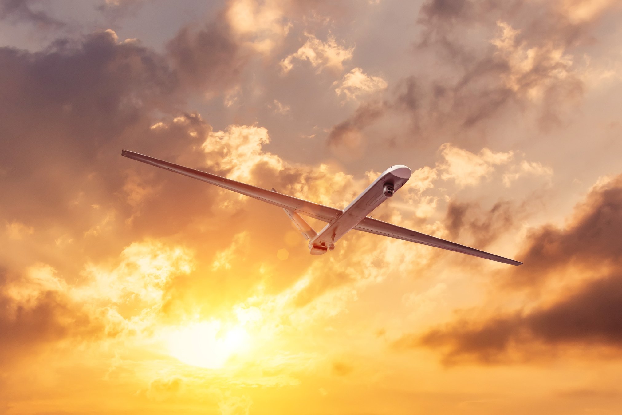 Unmanned military drone flies the at sunset clouds sky.